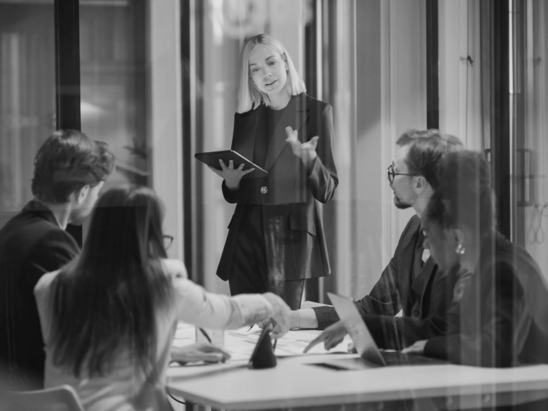 A woman hosting a meeting to four people in an office setting